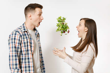 Fun couple man woman standing and throwing up salad from glass bowl isolated on white background....