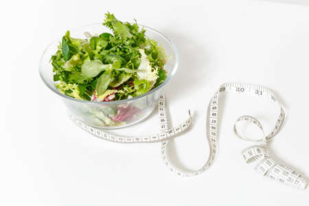Close up green vegetables salad in glass bowl, tailor measuring tape isolated on white background.の写真素材