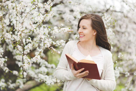 Young smiling charming beautiful woman in light casual clothes reading interesting book standing in...