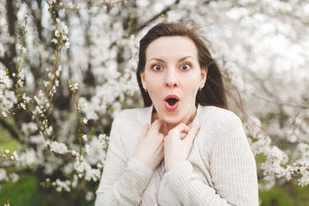 Young brunette shocked beautiful woman in light casual clothes clinging to chest standing in city...