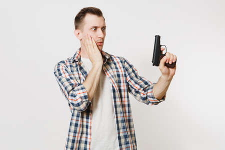 Shocked sad upset young man with gun in hand isolated on white background.