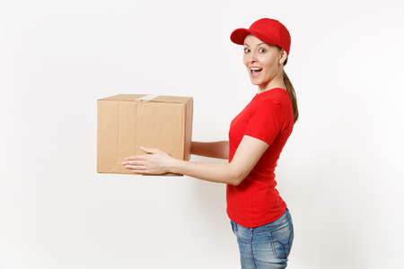 Delivery woman in red uniform isolated on white background. Female in cap, t-shirt, jeans working as courier or dealer holding cardboard box. Receiving package. Copy space advertisement. Side viewの写真素材