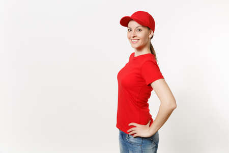 Delivery woman in red uniform isolated on white background side view. Professional female in cap, t-shirt, jeans working as courier or dealer standing and looking aside. Copy space advertisementの写真素材