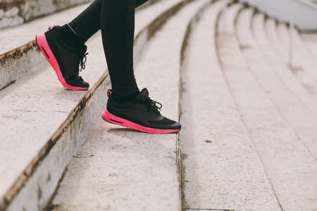 Cropped photo close up of female legs in sportswear, black and pink woman sneakers doing sport exercises, going down on stairs outdoors. Fitness, healthy lifestyle concept. Copy space advertisementの写真素材