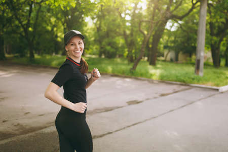 Young athletic smiling beautiful brunette girl in black uniform and cap training, doing sport...
