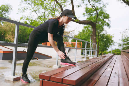 Young concentrated athletic brunette girl in black uniform, cap with headphones listening music...