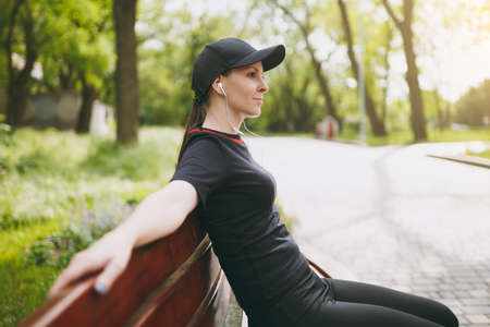 Young relaxed athletic pretty brunette girl in black uniform and cap with headphones resting after...