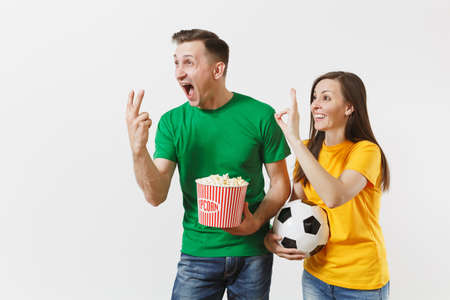 European young couple, woman, man, football fans in yellow green t-shirt cheer up support team with soccer ball bucket of popcorn isolated on white background. Sport family leisure, lifestyle conceptの写真素材