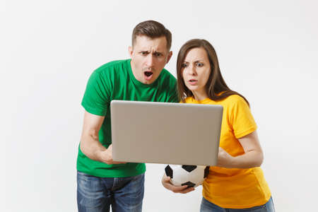 Shocked couple woman man, football fans in yellow green t-shirt cheer up support team with soccer ball, watching game on pc laptop isolated on white background. Sport family leisure lifestyle conceptの写真素材