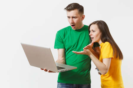 Shocked couple woman man, football fans in yellow green t-shirt cheer up support team with soccer ball, watching game on pc laptop isolated on white background. Sport family leisure lifestyle conceptの写真素材