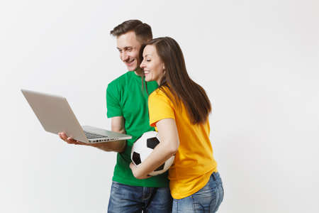 Young couple, woman man, football fans in yellow green t-shirt cheer up support team with soccer ball, watching game on pc laptop isolated on white background. Sport family leisure lifestyle conceptの写真素材