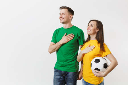 Emotional couple, woman man, football fans in yellow green t-shirt cheer up support team with soccer ball singing national country anthem isolated on white background. Sport leisure lifestyle conceptの写真素材