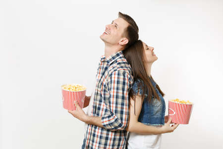 Young happy smiling couple, woman and man in 3d glasses and casual clothes watching movie film on date, holding buckets of popcorn, relaxing isolated on white background. Emotions in cinema conceptの写真素材
