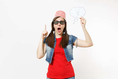 Portrait of Surprised woman in 3d glasses with bucket for popcorn on head watching movie film holding say cloud lightbulb, idea and pointing finger up isolated on white background. Emotions in cinemaの写真素材
