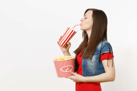 Portrait of young beautiful woman with closed eyes watching movie film, holding bucket of popcorn,...