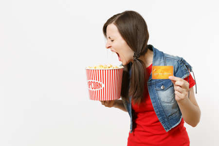 Portrait of young crazy loony brunette woman in casual clothes watching movie film, holding bucket of popcorn and credit card, screaming isolated on white background. Emotions in cinema conceptの写真素材