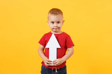 Little cute kid baby boy 3-4 years old in red t-shirt holding in hand up arrow isolated on yellow background. Kids childhood lifestyle concept. Appreciation of exchange rates. Copy spaceの写真素材