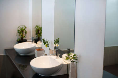Two modern ceramic washbasins with mirrors in the restroom of the restaurant. Ceramic sink with...