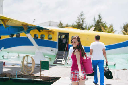 A beautiful European girl in sunglasses, a pink T-shirt and shorts goes on boarding a water plane on a pier in the Indian Ocean in the Maldives to get to the island for a rest on vacationの写真素材