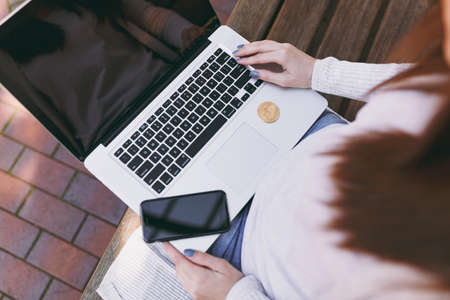 Close up female hands on keyboard. Woman sitting on bench working on modern laptop with blank empty screen to copy space. Bitcoin in street outdoors. Mobile Office, virtual future currency conceptの写真素材