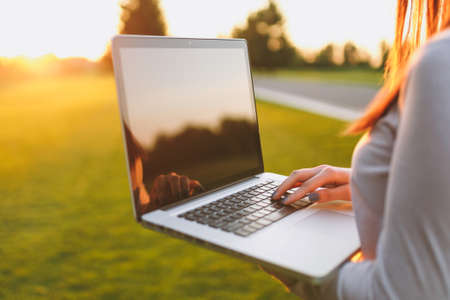 Close up hands on keyboard. Woman working on laptop pc computer with blank black empty screen to copy space in park on green grass sunshine lawn outdoors. Mobile Office. Freelance business conceptの写真素材