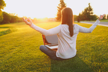 Young calm student female in casual clothes. Woman sitting, relaxing, hands in yoga gesture. Laptop...