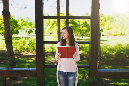 Portrait of beautiful calm peaceful young woman wearing light casual clothes relaxing, reading book. Smiling female resting in city park in street outdoors on spring nature. Lifestyle, conceptの写真素材