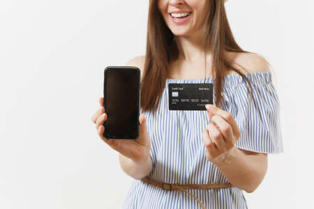 Cropped shot of woman in blue dress showing camera mobile phone with blank black empty screen, holding credit card isolated on white background. People, banking concept. Advertising area. Copy spaceの写真素材