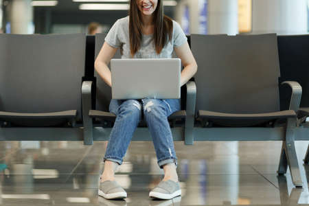 Cropped Young joyful traveler tourist woman working on laptop while waiting in lobby hall at international airport. Passenger traveling abroad on weekends getaway. Air travel, flight journey conceptの写真素材