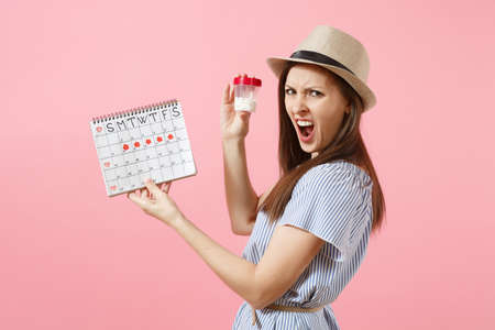Portrait of sad woman in blue dress holding white bottle with pills, female periods calendar, checking menstruation days isolated on background. Medical healthcare, gynecological concept. Copy spaceの写真素材