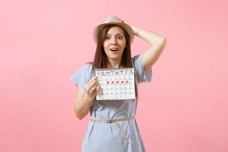 Portrait of young woman in blue dress, hat holding periods calendar for checking menstruation days isolated on bright trending pink background. Medical, healthcare, gynecological concept. Copy spaceの写真素材