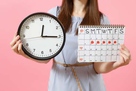 Cropped photo of woman in blue dress holding round clock, periods calendar for checking menstruation days isolated on trending pink background. Medical, healthcare, gynecological concept. Copy spaceの写真素材