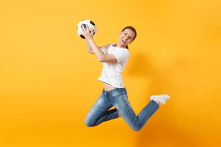 Young fun expressive European woman football fan jumping in air, cheer up support team, holding soccer ball isolated on yellow background. Sport, play football, cheer, fans people lifestyle conceptの写真素材