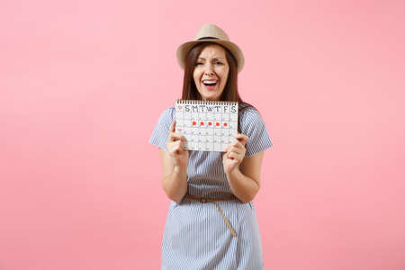 Portrait sad illness woman in blue dress holding periods calendar for checking menstruation days put hand on abdomen isolated on pink background. Medical healthcare, gynecological concept. Copy spaceの写真素材