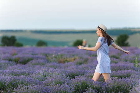 Portrait of young smiling beautiful woman in blue dress, hat on purple lavender flower blossom meadow field outdoors on summer nature, Provence. Happy female run at flowering bush. Lifestyle conceptの写真素材