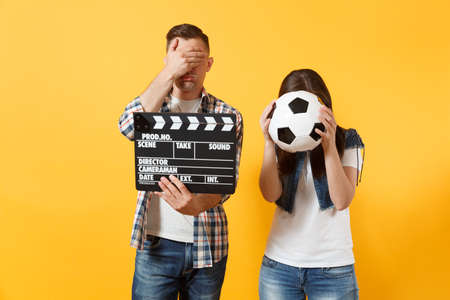 Young excited couple woman man football fans cheer up support team with soccer ball, film making clapperboard isolated on yellow background. Sport family leisure lifestyle concept. Cameraman studioの写真素材