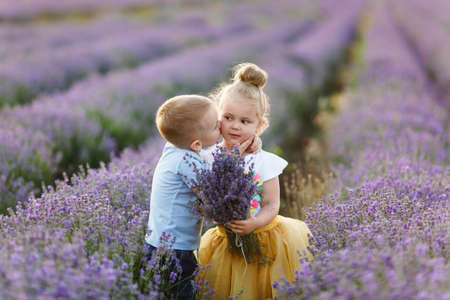 Playful little cute couple boy girl walk on purple lavender flower meadow field background, have fun, play, enjoy good sunny day. Excited small kids. Family day, children, childhood lifestyle conceptの写真素材
