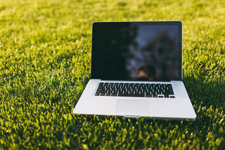 Close up laptop pc computer with blank black empty screen to copy space in park on vibrant spring green fresh grass, sunshine lawn meadow outdoors on nature. Mobile Office. Freelance business conceptの写真素材