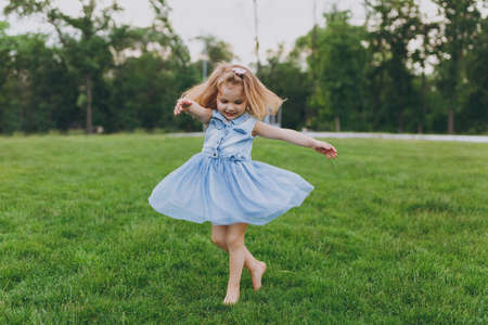 Pretty little cute child baby girl in denim dress circling around and have fun on green grass lawn in park. Mother, little kid daughter. Mother's Day, love family, parenthood, childhood conceptの写真素材