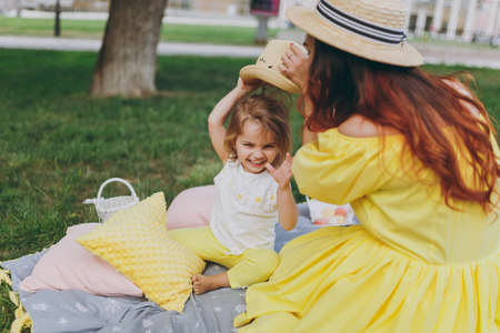 Woman in yellow clothes play on green grass lawn in park, rest and have fun with little cute child...