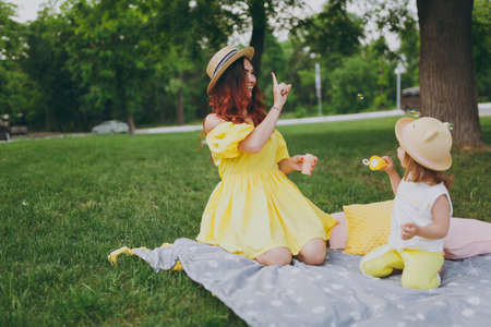 Smiling woman in yellow dress play in park, have fun and amuse with little cute child baby girl hold soap bubble blower. Mother, little kid daughter. Mother's Day, love family, parenthood, childhoodの写真素材