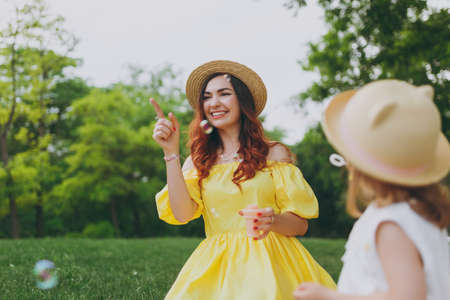 Joyful woman in yellow clothes play in park, rest and have fun with little cute child baby girl hold...