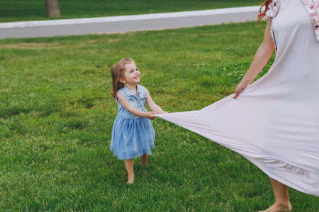 Little cute child baby girl running catching up have fun with joyful woman in light dress on green grass in park. Mother, little kid daughter. Mother's Day, love family, parenthood, childhood conceptの写真素材