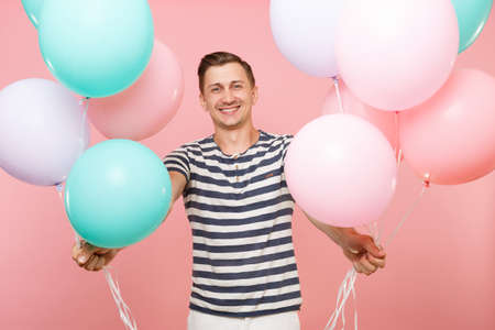 Portrait of fascinating young happy man wearing striped t-shirt holding colorful air balloons isolated on bright trending pink background.の写真素材