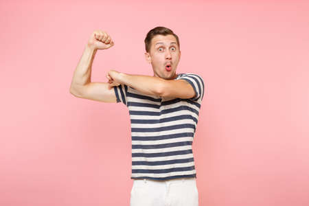 Portrait of strong young hipster man dresssed casually in striped tshirt showing biceps muscles isolated on trending pink background.の写真素材