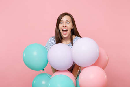 Portrait of overjoyed young happy woman with opened mouth in blue dress hold colorful air balloons isolated on bright trending pink background. Birthday holiday party, people sincere emotions conceptの写真素材