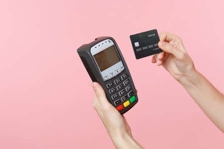 Close up cropped photo of female holding in hands wireless modern bank payment terminal to process and acquire credit card payments, black card isolated on pink background. Copy space for advertisingの写真素材