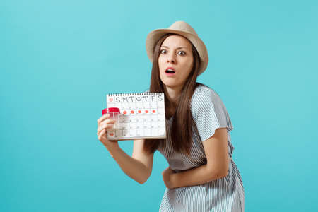 Portrait of sad woman in dress holding white bottle with pills, female periods calendar, checking menstruation days isolated on blue background. Medical healthcare, gynecological concept. Copy spaceの写真素材