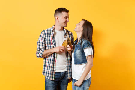 Young smiling couple woman and man sport fans in casual clothes cheer up support team clinking beer bottles looking at each other isolated on yellow background.の写真素材