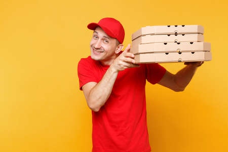 Delivery man in red cap, t-shirt giving food order pizza boxes isolated on yellow background. Male employee pizzaman or courier in uniform holding italian pizza in cardboard flatbox. Service conceptの写真素材